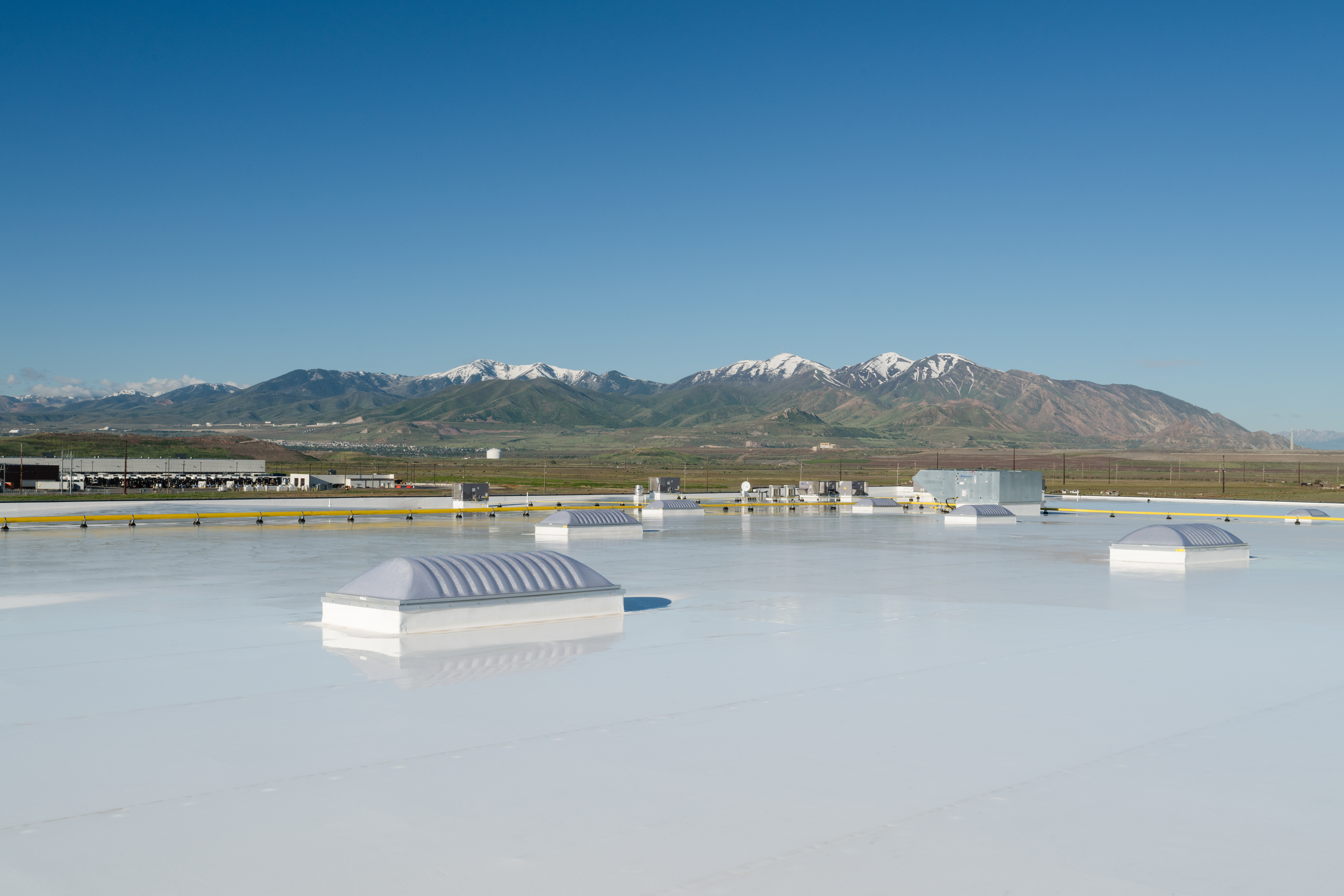 Rooftop view featuring an UltraPly TPO roofing system with a smooth, reflective surface. The background showcases a scenic mountain range with snow-capped peaks under a clear blue sky, highlighting the durability and performance of the UltraPly TPO membrane in diverse climates.